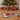 Two red pet bowls with food on a bone-shaped mat in front of a Christmas tree and presents.