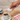 Hand pouring milk from a small white pitcher into a cup of coffee on a wooden table.