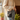 Person wearing a beige sweater and blue jeans holding a black handbag with a paw print charm.