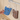 Blue and brown dog-shaped scrubber hanging on a hook with a hand holding the blue one.