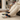A person sitting on a couch in a cozy living room, wearing cream knit pants and slip-on slippers with a colorful cartoon print and dark navy fuzzy trim. A fireplace burns in the background, and a white cable-knit blanket is draped over the armrest.